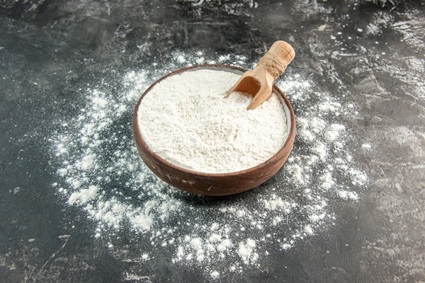front close view of white flour with wooden spoon inside and outside of brown bowl on gray background - Соус с яйцом
