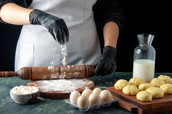front view female cook rolling out dough with flour on dark job cuisine hotcake raw dough bake cake pie worker egg - Пирожки дрожжевые печёные