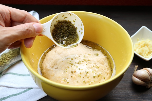 hand pouring olive oil with herbs onto kneaded dough for baking italian focaccia bread - Фокачча с помидорами и луком