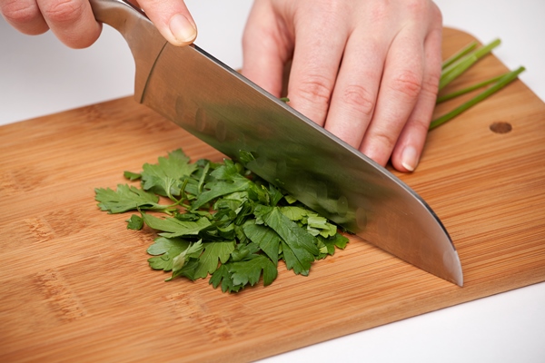 hand with a kitchen knife cuts and chops parsley on a wooden cutting board - Острая закуска из шампиньонов