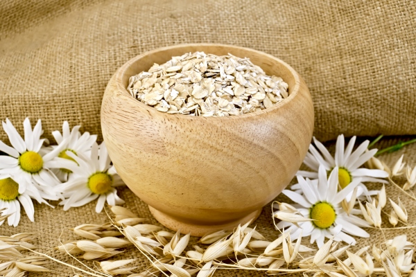 oat flakes in a wooden bowl stalks of oats chamomile on burlap and wooden board - Монастырская кухня: смоленская каша с овощами, лимонный кисель