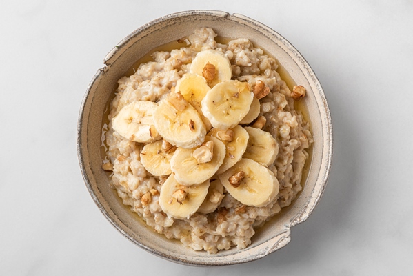 oatmeal porridge with banana walnuts and honey in a bowl on white background top view - Овсянка с какао без варки