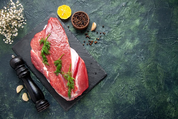 overhead view of green on fresh red raw meat on cutting board and pepper lemon wooden hammer flower on the right side on green black mix color background - Ростбиф