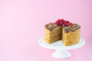 pancake cake with chocolate caramel nuts and raspberries on a pink wall 1 - Блинный торт с карамелью и орехами