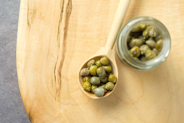 pickled or marinated green capers on a wooden spoon close up selective focus - Соус с каперсами