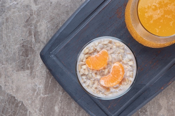 porridge with two orange slices in a glass on a wooden tray next to orange juice on the marble background - Овсянка без варки с мандарином