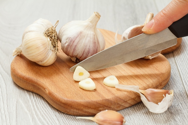 ripe garlic and a hand with a stainless steel knife on a wooden cutting board - Монастырская кухня: печенье на томатном соке, овсяный суп с цветной капустой