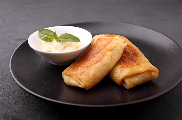 rolled crepes with meat and sauce served on black plate - Блинчики с мясом