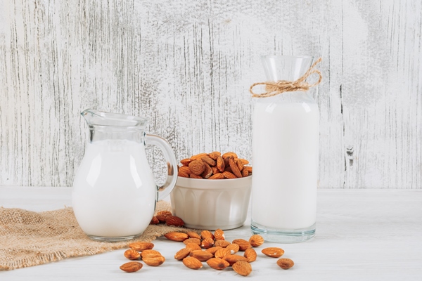 side view milk carafe with bowl of almonds and bottle of milk on white wooden and piece of sack background horizontal - Овсянка с бананом без варки