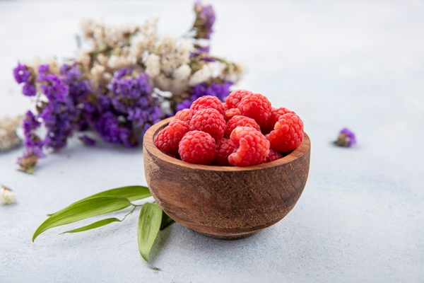 side view of raspberries in bowl with flowers and leaves on white - Овсянка с бананом без варки