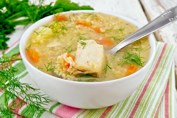 soup fish kulesh with millet potatoes and carrots and spoon in a bowl on a napkin parsley dill on a wooden board background - Монастырская кухня: грибной бульон с расстегаями, кулеш