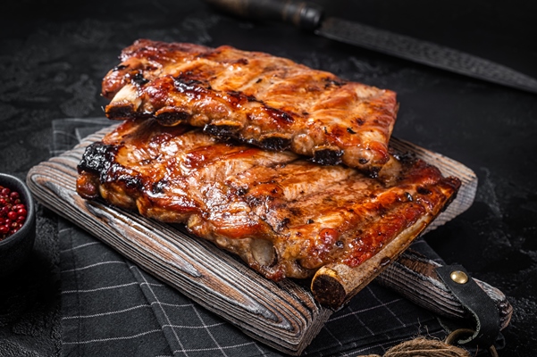 stack of grilled pork ribs in bbq sauce on a chopping board black background top view - Печень жареная