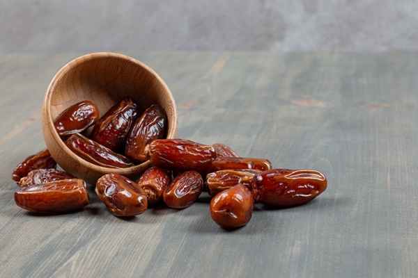 sweet dates out of wooden bowl on marble surface - Урбеч с какао и финиками