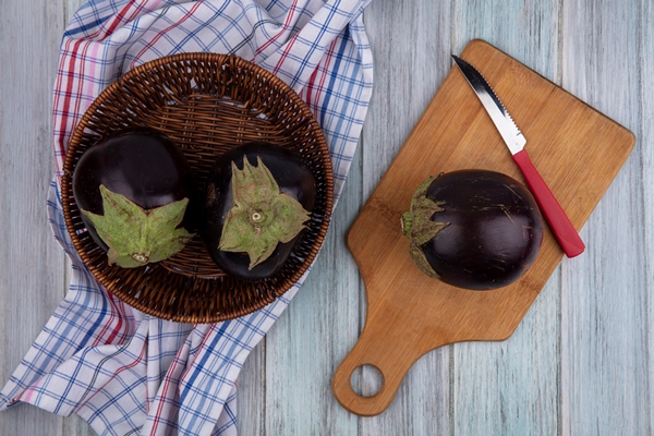 top view of eggplants with knife on cutting board and in basket on plaid cloth on wooden background 1 - Монастырская кухня: овсяная каша, закуска из баклажанов