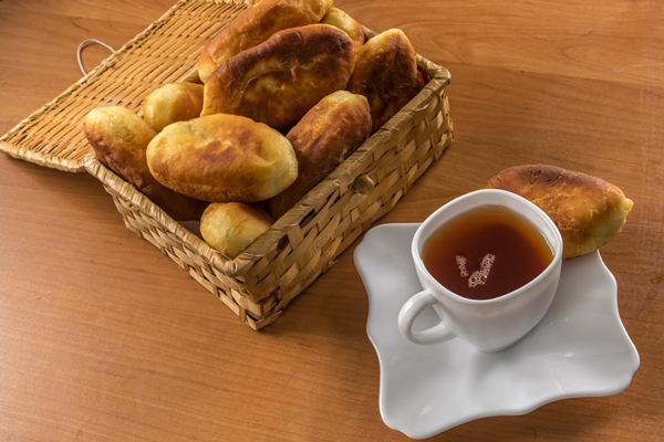 traditional homemade baked patties or pies with jam in a wicker basket next to a white cup of tea - Монастырская кухня: пшённые биточки с грибами, жареные пирожки с повидлом