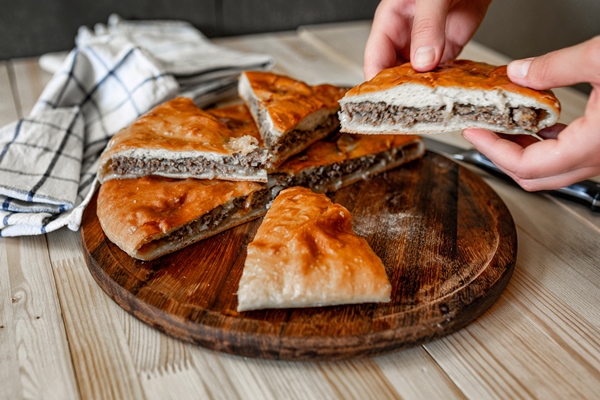 traditional ossetian meat pies with beef on a wooden table rustic style close up selective focus - Пирог печёный из дрожжевого теста