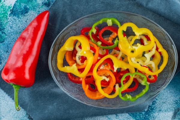 various sliced peppers in a bowl next to red peppers on a pieces of fabric on the blue background - Монастырская кухня: овощи в кляре, морковные клёцки
