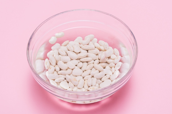 white beans soaked in water in glass bowl on pink background - Хумус из фасоли с грибами