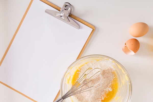 white blank paper on clipboard with whipped egg and flour bowl on white backdrop - Блинцы на ряженке