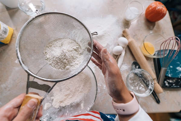 woman s hands sifting flour through sieve selective focus - Блинчики с луком и яйцом