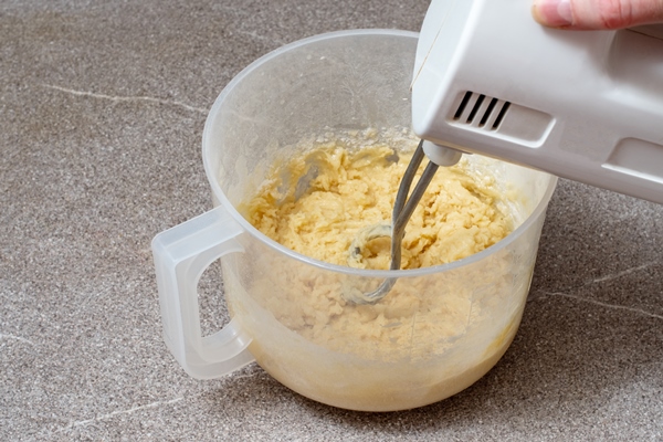 a hand holds a mixer for beating dough in a plastic bowl kneading dough in a mixer homemade baking concept - Пасхальная мона