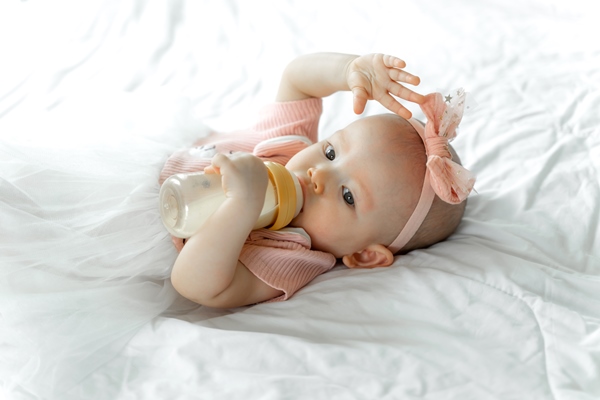 baby drinks milk from a bottle on a white bed - Особенности питания детей