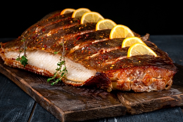 baked halibut fish with lemon on wooden board on dark surface - Камбала или палтус, запечённые в духовке