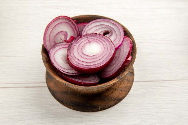 bottom view chopped red onion in wooden bowl on white table - Запечённый морской окунь с картофелем