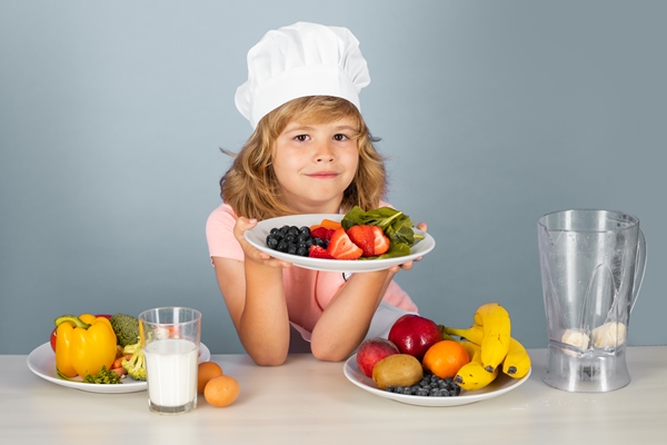 child chef hold plate with fruits isolated on blue funny little kid chef cook wearing uniform cook cap and apron cooked food in the kitchen - Особенности питания детей