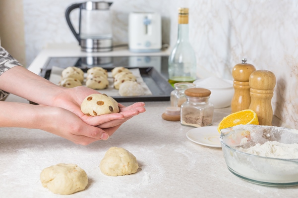 close up of preparing and forming easter cross buns with raisins out of dough female hands kneading dough in modern minimalistic kitchen - Пасхальные крестовые булочки