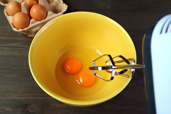 closeup of electric egg beater going to beat apair of raw eggs in mixing bowl - Пасха без творога с изюмом