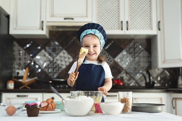 cute little girl in an apron and a chef s hat is stirring the dough with a wooden spatula - Кулич быстрый с лимоном и ванилином