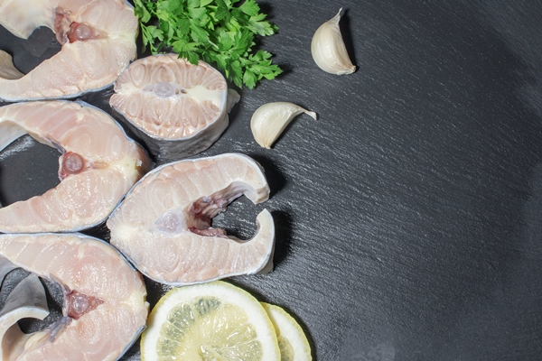delicious raw fresh sturgeon steaks with lemon parsley and garlic on black copy space - Буглама из рыбы
