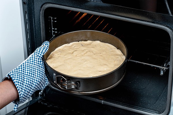 female hand puts a baking tray with dough in the oven - Марципановый кулич симнель