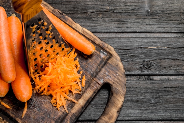 grated carrots on a cutting board with a grater on wooden background - Монастырская кухня: рисовая каша с морковью, печенье макруд