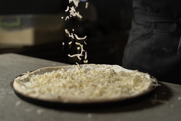grated hard cheese lays on the pizza the process of cooking in production in a pizzeria - Пасхальный каравай "Касатьелло"