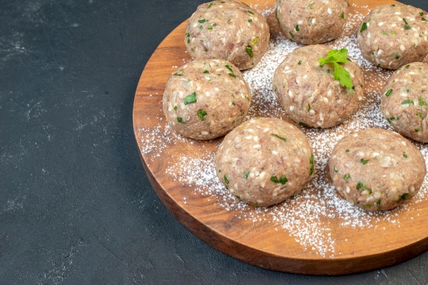 half shot of uncooked meat balls with green in a brown plate on the left side on black background with free space - Зразы мясные, паровые, фаршированные омлетом