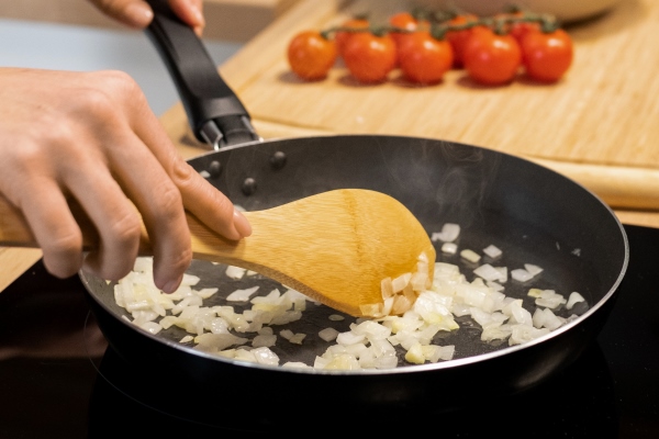 hands of young woman mixing chopped onion in frying pan - Ризотто постное с икрой