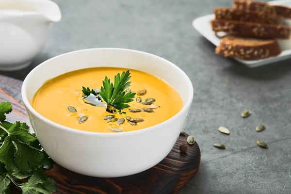 pumpkin and carrot chowder with olive oil in a white cup pumpkin seeds and parsley on a gray background close up on seasonal vegetarian soup selective sharpening on parsley - Лечебный стол (диета) № 1 по Певзнеру: таблица продуктов и режим питания
