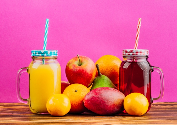 red and yellow juice mason jars with drinking straws and fresh fruits against pink background - Особенности питания детей