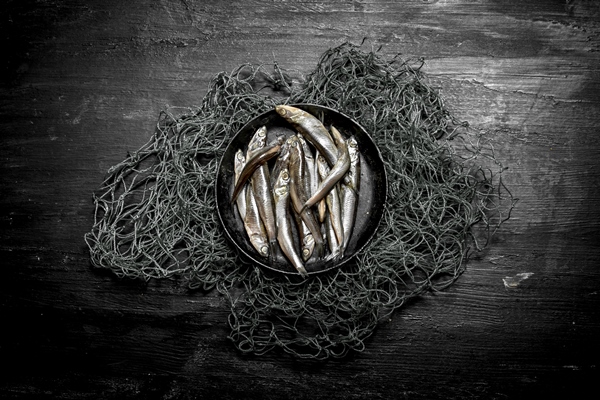 sprats in a bowl on the fishing net on a black wooden background - Шкара классическая
