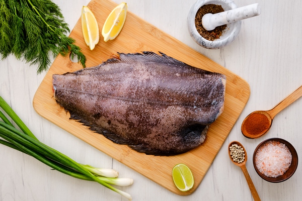 top view of raw fresh halibut without head on wooden cutting board - Камбала или палтус, запечённые в духовке