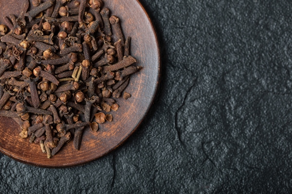 a brown plate full of dried cloves on a dark background - Маринованные бутоны черемши