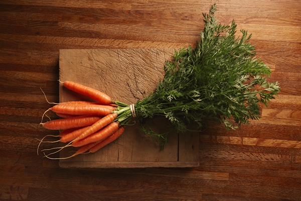 a bunch of fresh carrots on a weathered old cutting board with deep cuts on a beautiful wooden brown table top view - Салат из одуванчиков с морковью и редисом