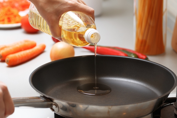 a woman pouring oil from a bottle into the pan in the kitchen near fresh vegetables and pasta 1 - Жареная черемша