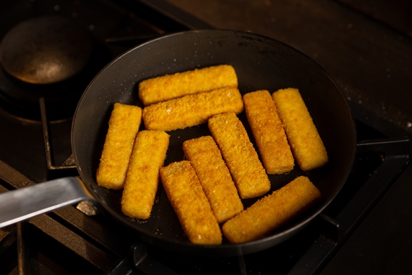 breaded fish sticks in a frying pan preparation of frozen fish sticks fast food dark background - Сырные палочки с черемшой