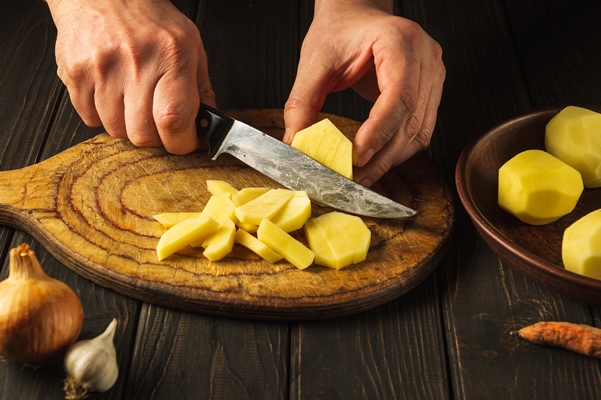 chef prepares raw potatoes for lunch or dinner closeup of cook hands while working in a kitchen - Картофель, жаренный с черемшой и яйцом