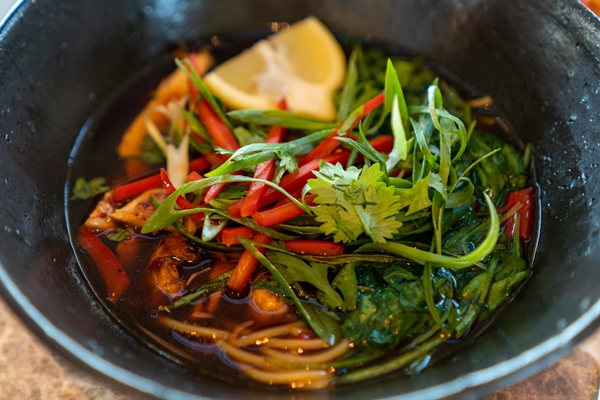 closeup shot of soup with vegetables lemon and greens in a black plate - Черемша по-корейски