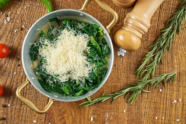 dietary food stewed spinach in a creamy garlic sauce with parmesan cheese in a decorative pan on wooden table in composition with spices 1 - Сныть отварная с сыром