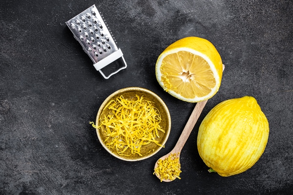 peeling lemon rind to add zest to mediterranean recipes grater peel and lemon zest on black background long banner format top view - Хумус с черемшой